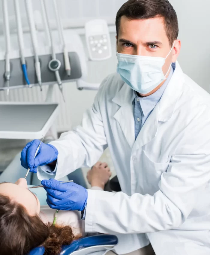 A dentist with a facemask checking his patients teeth.